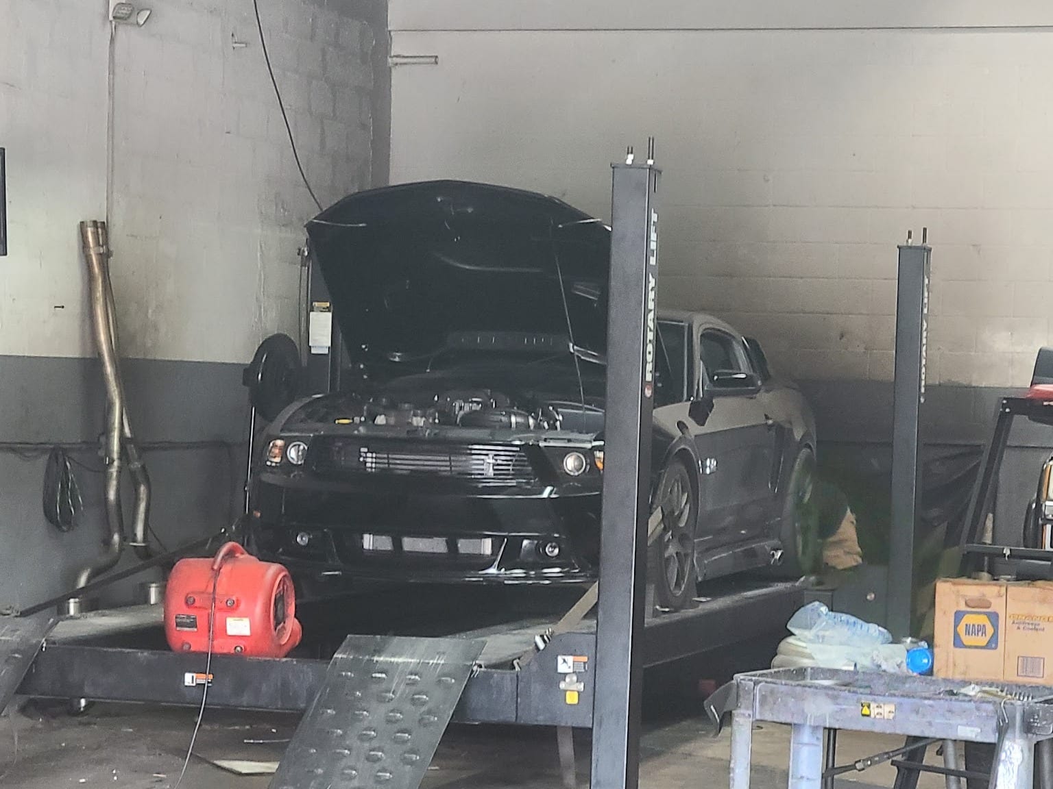 A black car on a lift with the hood up in a Custom Speed Creations bay