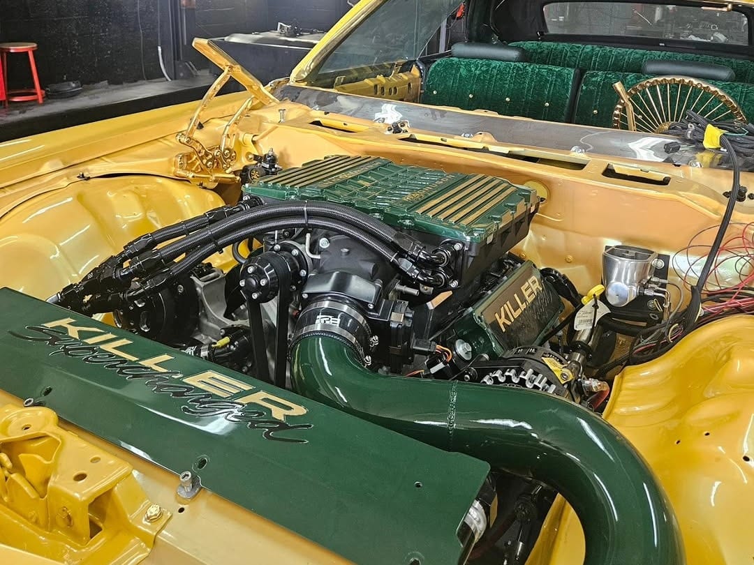 The engine bay of a yellow classic convertible with a green KILLER intake, in the Custom Speed Creations shop