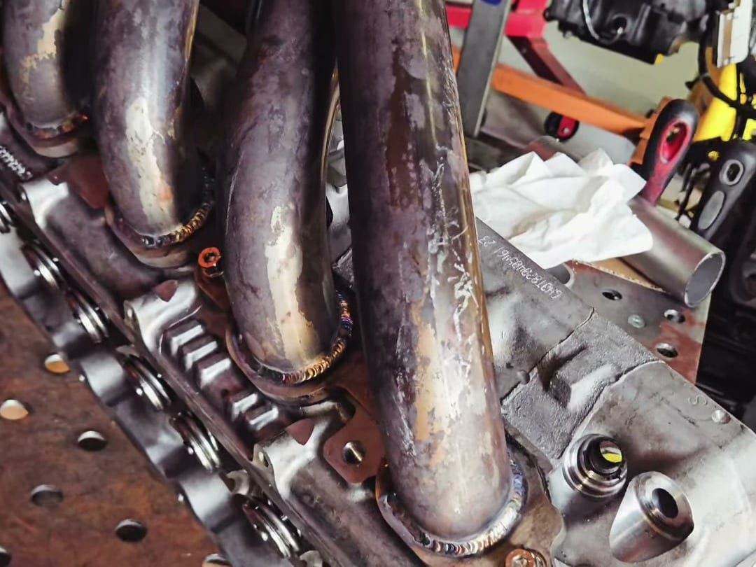 A long-tube header from an LT1 Camaro bolted to a cylinder head on the welding table, with fresh welds at the flange