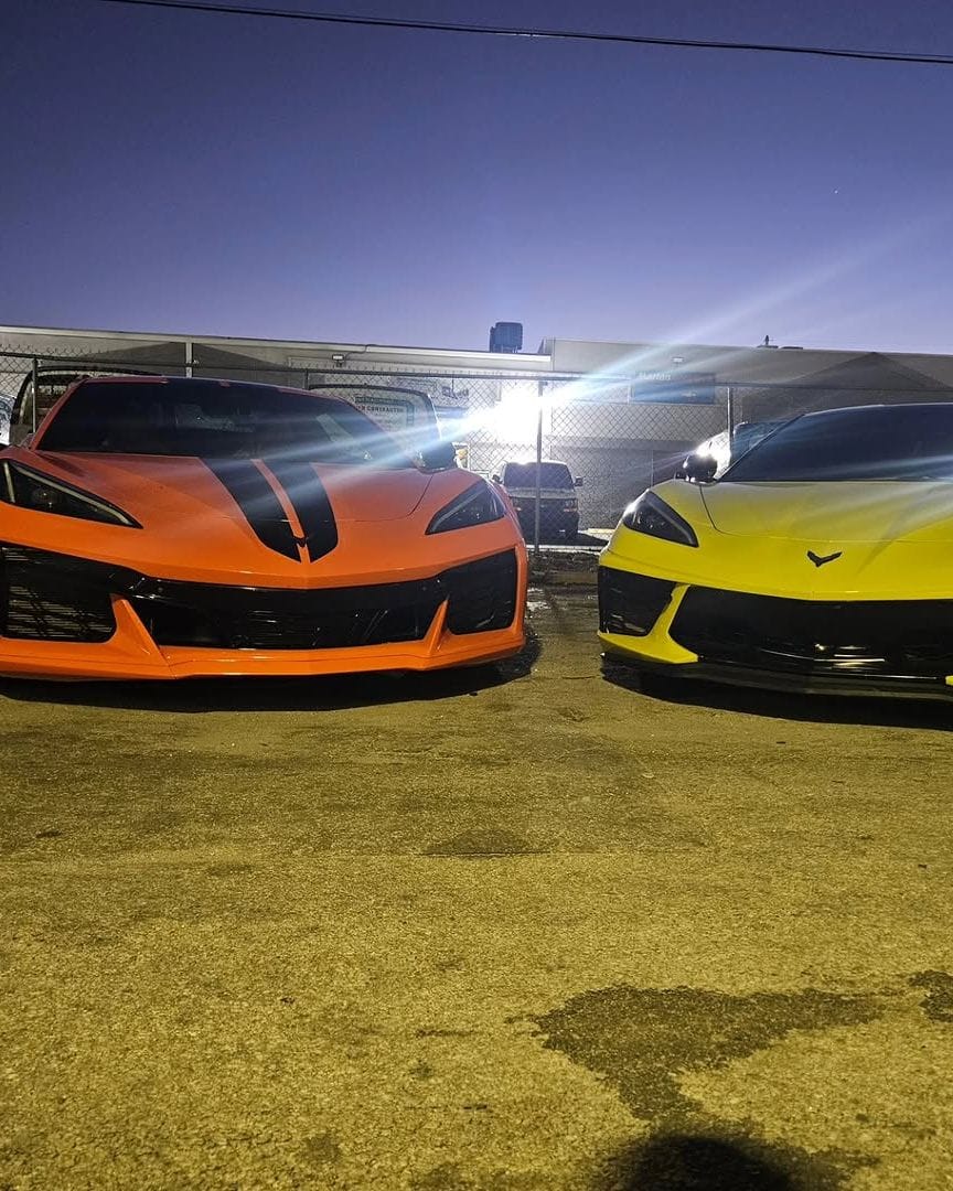 An orange C8 Corvette with black stripes parked beside a yellow C8 Corvette at dusk