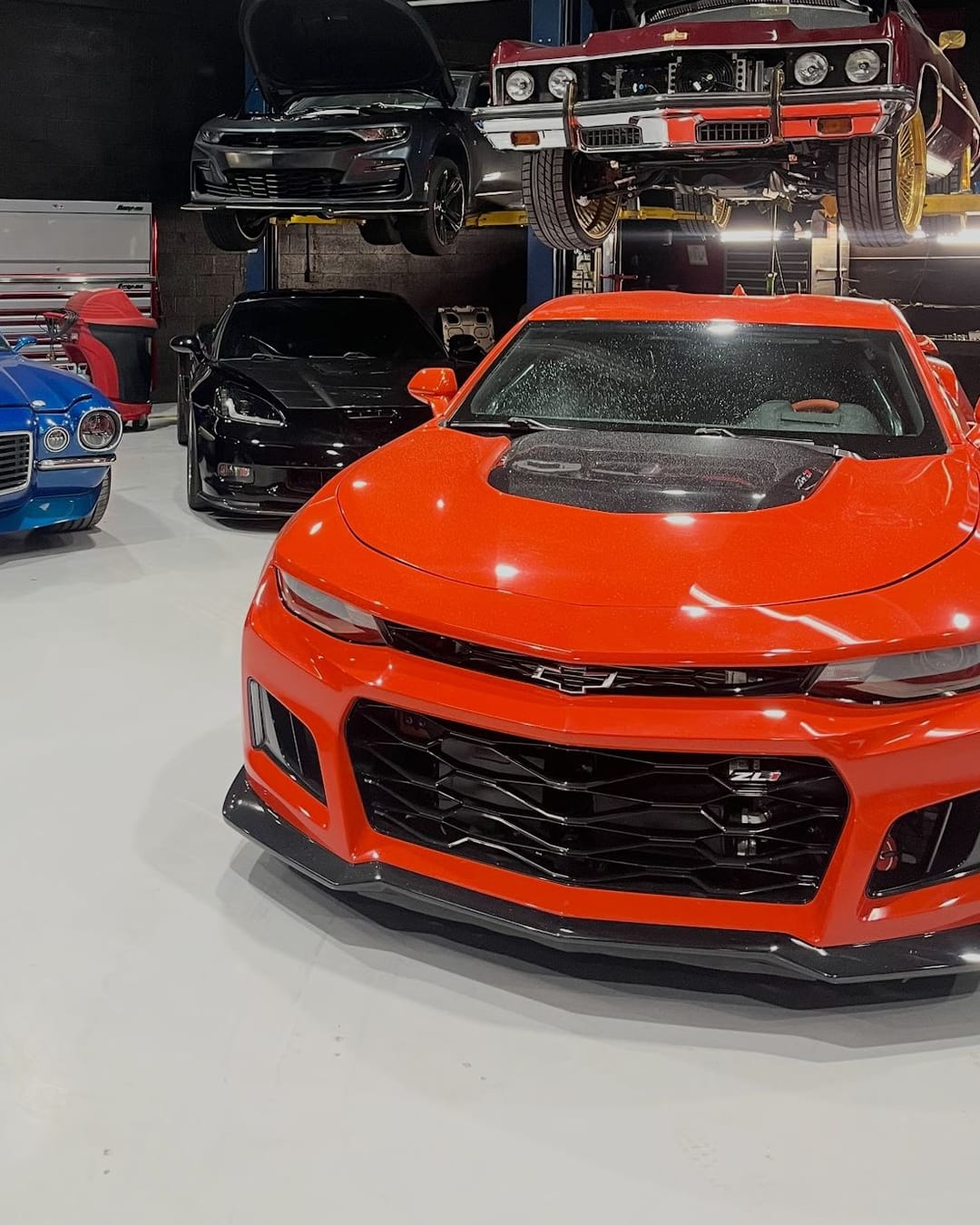 An orange sixth-generation Camaro ZL1 beside a blue second-generation Camaro on the Custom Speed Creations shop floor, with a classic on the lift behind them