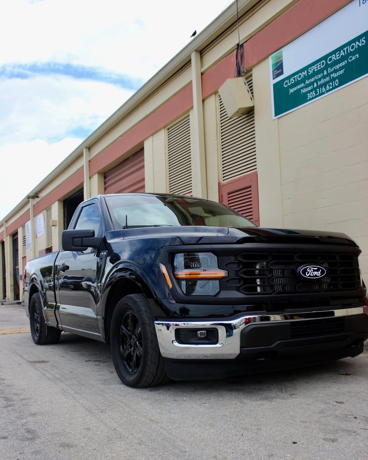 A lowered black Ford F-150 parked outside Custom Speed Creations, under the shop sign